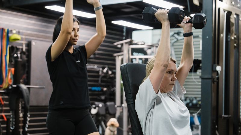Personal trainer guiding a client in the gym, demonstrating proper form.