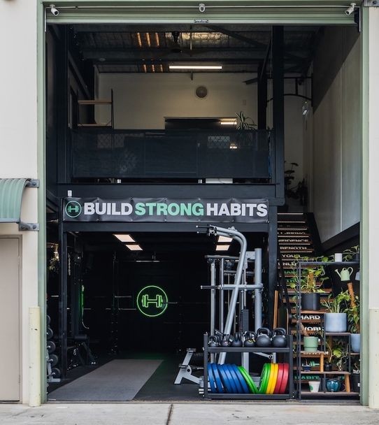 Habitat Gym front view showing open roller door, visible signage, and weights set up outside