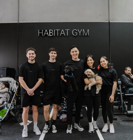 The Habitat Gym team lined up in matching black shirts beneath the Habitat Gym sign, two of them cradling dogs