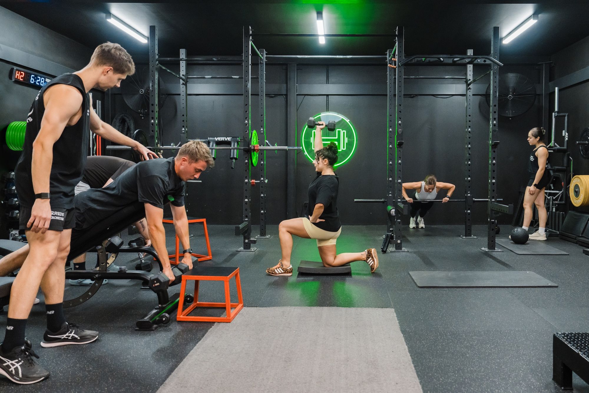 Coach supervising clients performing dumbbell rows, kneeling presses, and squats during a semi-private session at Habitat Gym in Prestons