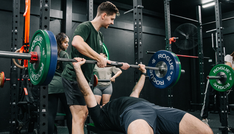 Personal trainer guiding a gym member doing bench press at Habitat Gym