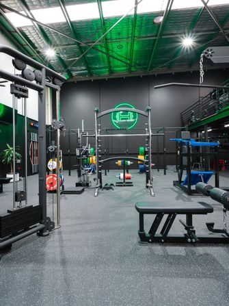 Cable stations, a power rack and adjustable benches beneath the green neon dumbbell sign in Habitat’s private Prestons gym