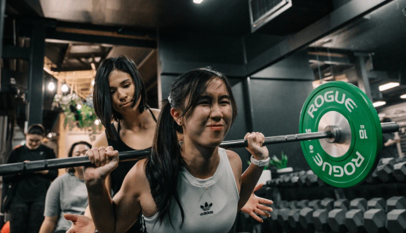 Coach Jeannie spotting a gym member during a weightlifting session at Habitat Gym