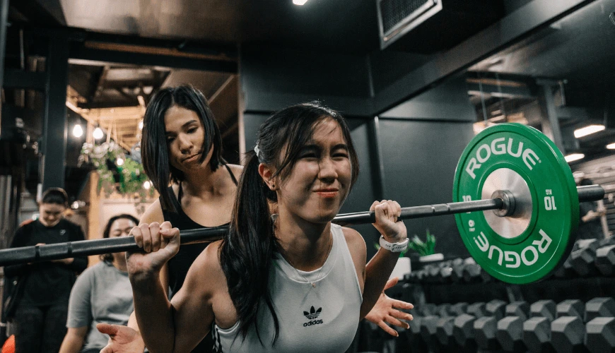 Coach Jeannie spotting a gym member during a weightlifting session at Habitat Gym