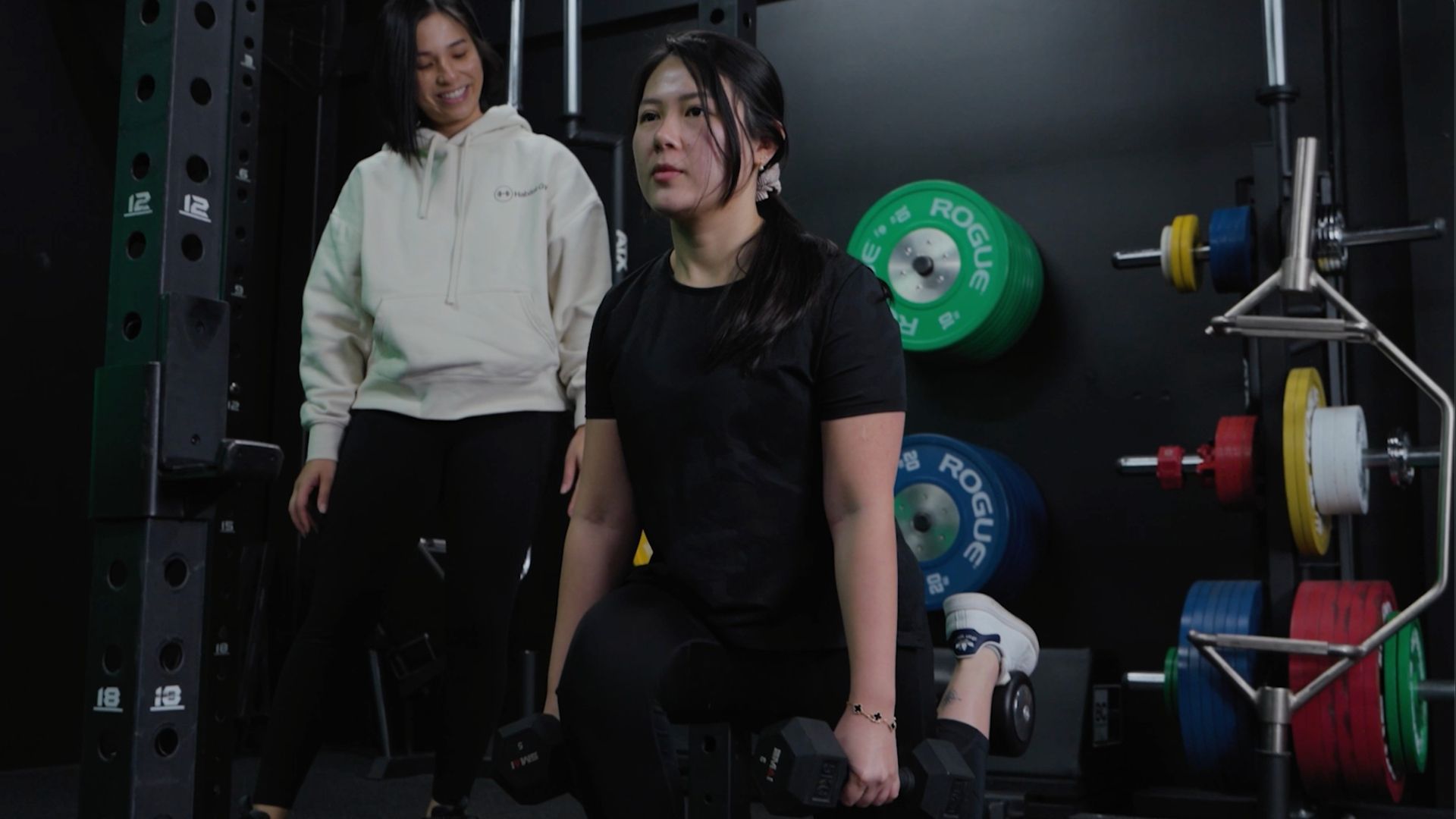 Lily doing a split squat with dumbbells at Habitat Gym in Prestons while her personal trainer watches on, smiling.