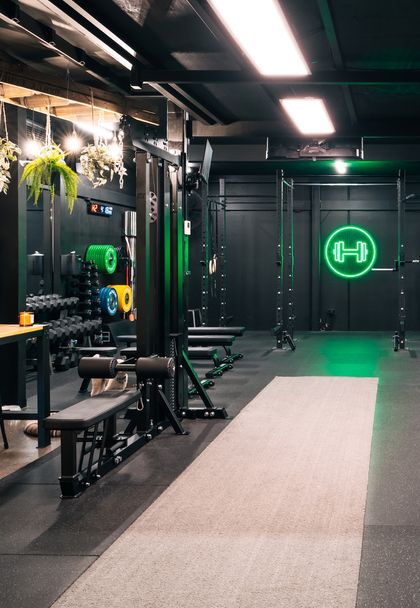 Strength training equipment arranged neatly below the glowing barbell neon sign at Habitat Gym
