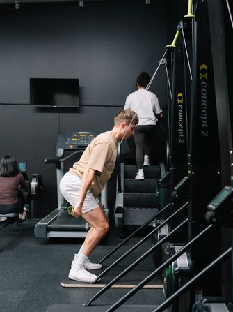 Member mid-pull on the Concept2 SkiErg while others work the stair climber and treadmill behind him at Habitat Gym