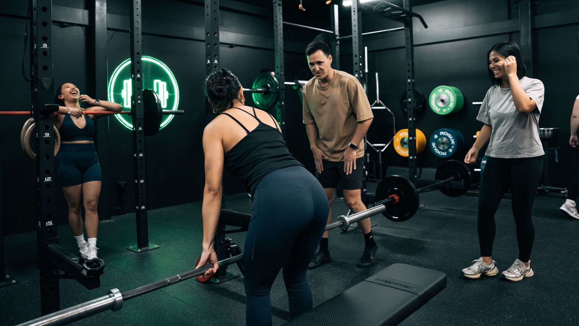 Personal trainer guiding a client during a strength training session in the gym, focusing on proper form and technique while other members share an encouraging moment.
