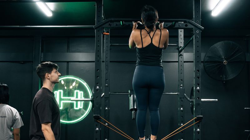 Personal trainer coaching a client through assisted pull-ups during a strength training session, focusing on proper form and control.