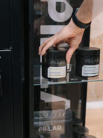 Hand reaching for a jar of Pillar Performance magnesium on the supplement shelf in Habitat Gym’s retail cabinet
