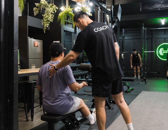 Habitat Coach correcting a gym members form whilst they are training on an assisted weight machine inside Prestons private gym
