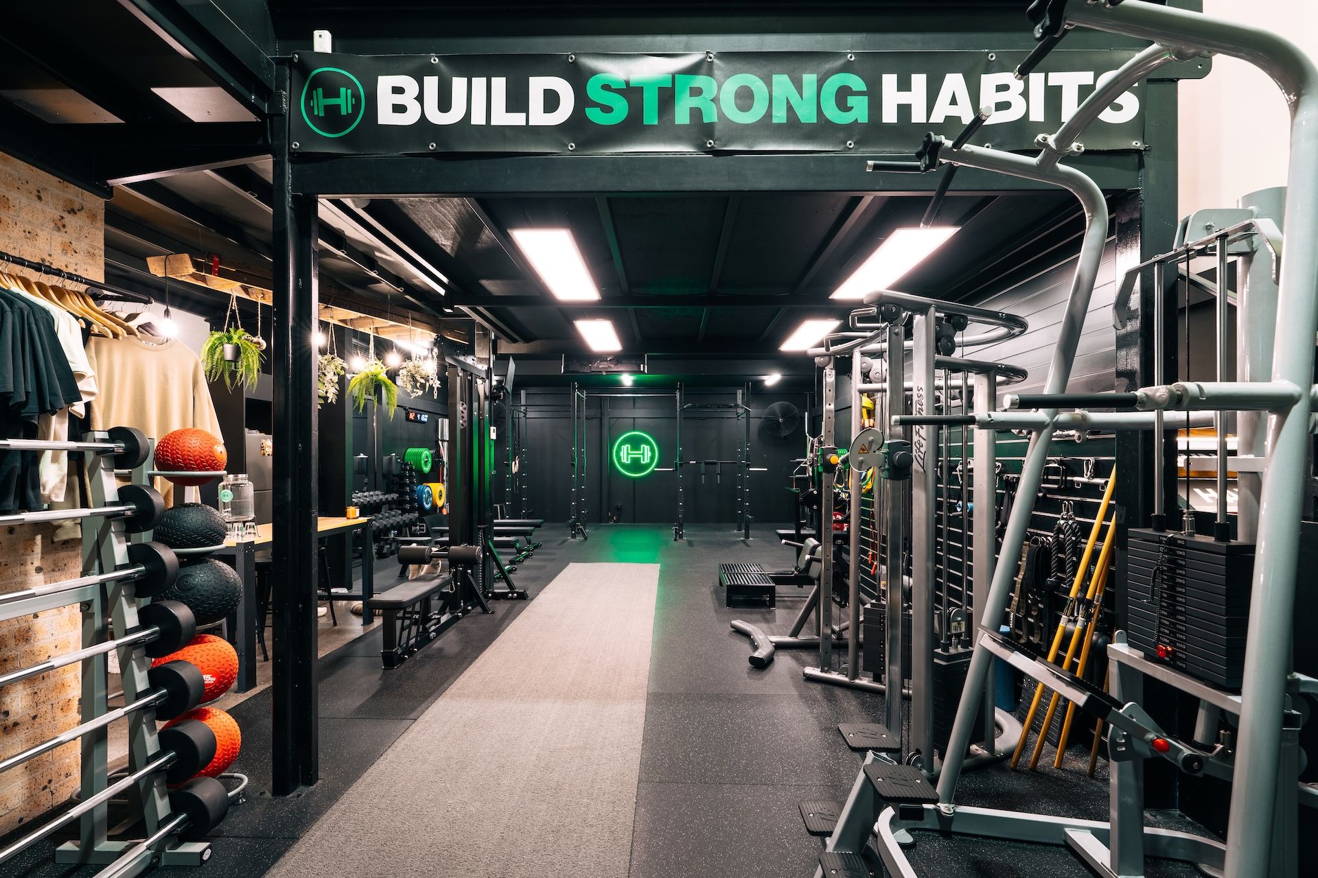 Wide-angle view of Habitat Gym’s ground floor with strength gear and “Build Strong Habits” banner