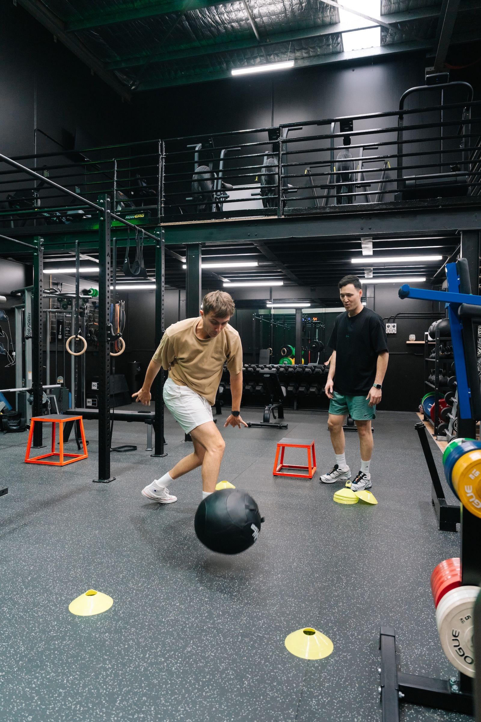 Coach watching a member work through an agility drill with a slam ball, marker domes and plyo boxes during a conditioning session at Habitat Gym