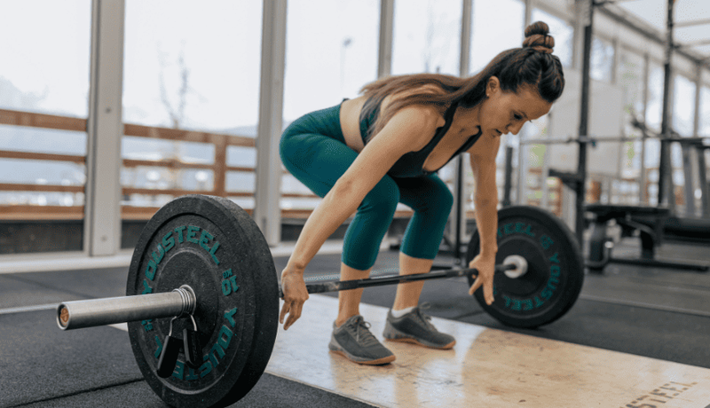 Woman lifting barbell inside a gym during strength training workout