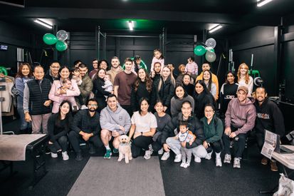 Members, families, and staff celebrate the opening of Habitat Gym, gathered together inside the facility decorated with green and white balloons