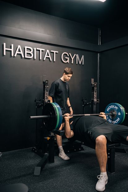 Personal trainer spotting a man performing a heavy barbell bench press at Habitat Gym