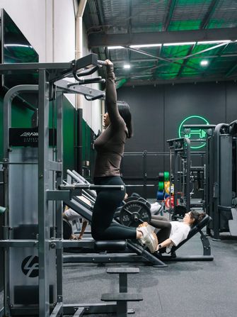 Member knocking out assisted chin-ups while others train on the leg press behind her at Habitat Gym